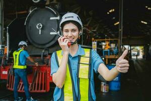 Beautiful woman engineer in factory talking on the radio wearing white helmet and work clothes photo