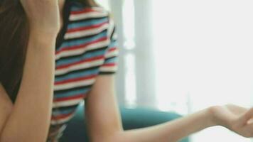 Happy Asian teen girl holding pad computer gadget using digital tablet technology sitting on the couch at home. Smiling young woman using apps, shopping online, reading news, browsing internet on sofa video