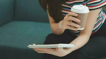 Happy Asian teen girl holding pad computer gadget using digital tablet technology sitting on the couch at home. Smiling young woman using apps, shopping online, reading news, browsing internet on sofa video