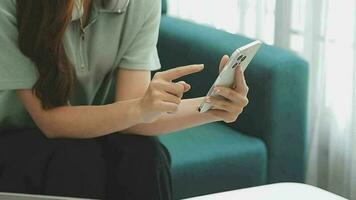 Happy Asian teen girl holding pad computer gadget using digital tablet technology sitting on the couch at home. Smiling young woman using apps, shopping online, reading news, browsing internet on sofa video