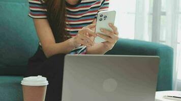 Happy Asian teen girl holding pad computer gadget using digital tablet technology sitting on the couch at home. Smiling young woman using apps, shopping online, reading news, browsing internet on sofa video