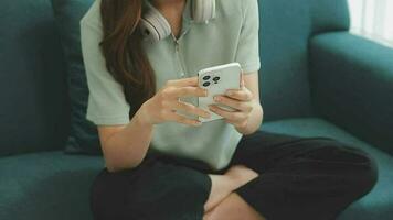 Happy Asian teen girl holding pad computer gadget using digital tablet technology sitting on the couch at home. Smiling young woman using apps, shopping online, reading news, browsing internet on sofa video