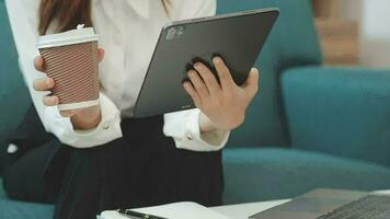 contento asiatico adolescente ragazza Tenere tampone computer aggeggio utilizzando digitale tavoletta tecnologia seduta su il divano a casa. sorridente giovane donna utilizzando app, shopping in linea, lettura notizia, navigazione Internet su divano video