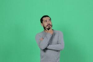 barbado asiático hombre poses vistiendo un gris camisa en contra un verde antecedentes foto