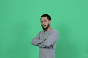 barbado asiático hombre poses vistiendo un gris camisa en contra un verde antecedentes foto