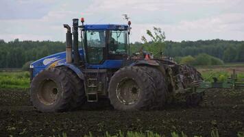 Blue New Holland tractor with double wheels pulling harrow at spring day with slow motion video