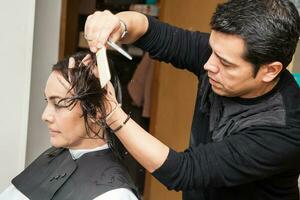 masculino estilista haciendo un Corte de pelo a un blanco mujer foto