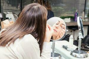 White woman removing makeup in front of mirror at beauty salon photo