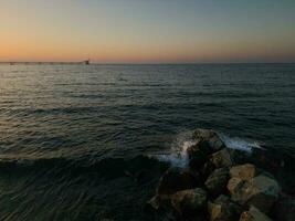 Seascape with crushing waves and old deserted industrial jetty in the distance at sunset at Karavostasi area near Lefka, Cyprus. photo