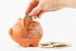 Close up of a woman saving money into a traditional clay piggy bank for a house photo
