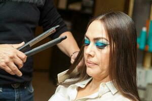 Stylist Using Flat Iron on Hair of Female Client Sitting in Salon Chair photo