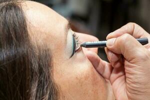 Makeup artist outlining white woman eyes photo