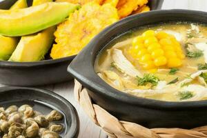Traditional Colombian ajiaco served with patacon, avocado and capers photo