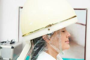Woman under a professional hair steamer with a hair treatment photo