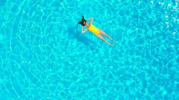 aéreo ver de un mujer en amarillo traje de baño nadando en el piscina. verano estilo de vida video