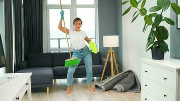 vrouw in hoofdtelefoons schoonmaak de huis en hebben pret dansen met een bezem en washandje video