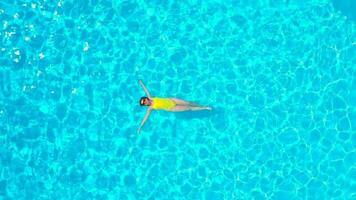 Aerial view of a woman in yellow swimsuit swimming in the pool. Summer lifestyle video