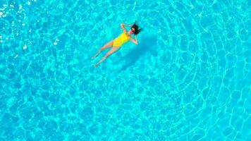 Aerial view of a woman in yellow swimsuit swimming in the pool. Summer lifestyle video