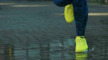 Female sports woman jogging outdoors, stepping into puddle. Single runner running in rain, making splash. Slow motion video