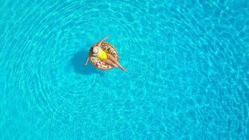 aéreo Visão do uma mulher dentro amarelo roupa de banho deitado em uma rosquinha dentro a piscina video