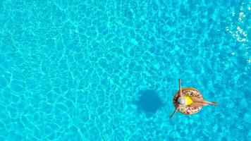 Aerial view of a woman in yellow swimsuit lying on a donut in the pool video