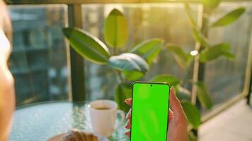 mujer sentado en un café y utilizando teléfono inteligente con verde Bosquejo pantalla en vertical modo. niña hojeada Internet video