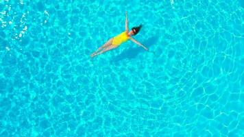 Aerial view of a woman in yellow swimsuit swimming in the pool. Summer lifestyle video