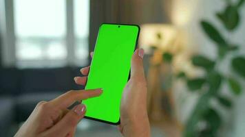mujer a hogar utilizando teléfono inteligente con verde Bosquejo pantalla en vertical modo. niña hojeada Internet, acecho contenido video