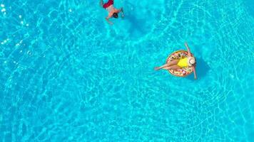 Haut vue de une couple ayant amusement dans le piscine, le homme nage et le femme mensonges sur un gonflable Donut video