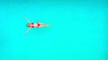 View from the top as a woman in red swimsuit lying on her back in the pool. Relaxing concept video