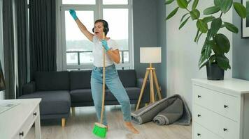 Woman in headphones cleans the house and have fun singing with a broom like a star at a concert video