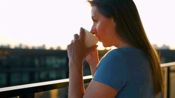 mujer con un taza de café en pie en el balcón y admirar el puesta de sol video