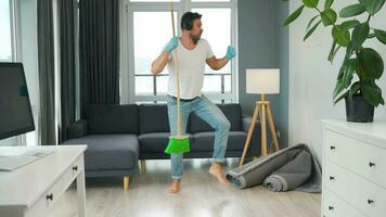 Man in headphones cleaning the house and fooling around with a broom video