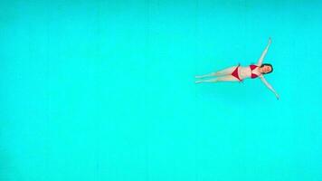 View from the top as a woman in red swimsuit lying on her back in the pool. Relaxing concept video