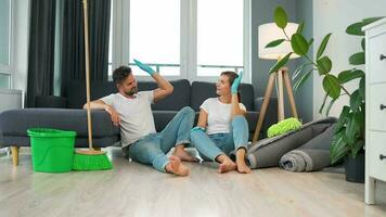 Tired couple sits on the floor in a room and high five each other after they finish cleaning the house video