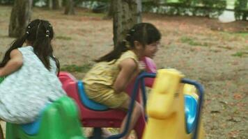 kinderen zitten Aan een carrousel in de speelplaats samen. kinderen spelen Bij buitenshuis speelplaats in de park Aan zomer vakantie. gezond werkzaamheid. video