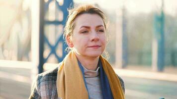 Portrait of a young caucasian businesswoman in a coat, walking across the bridge on a frosty sunny morning, drinking coffee and using smartphone. Communication, work day, busy life concept video