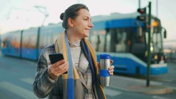 Woman in a coat standing on the street in the early morning and using smartphone video