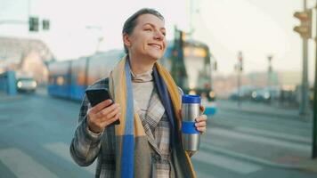 donna nel un' cappotto in piedi su il strada nel il presto mattina e utilizzando smartphone video