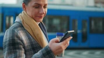 femme dans une manteau permanent sur le rue dans le de bonne heure Matin et en utilisant téléphone intelligent video