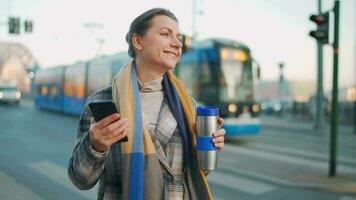 Woman in a coat standing on the street in the early morning and using smartphone video