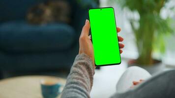 vrouw Bij huis gebruik makend van smartphone met groen mock-up scherm in verticaal modus. meisje browsen internetten, aan het kijken inhoud video