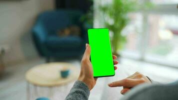 Woman at home using smartphone with green mock-up screen in vertical mode. Girl browsing Internet, watching content video