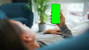 vrouw Bij huis gebruik makend van smartphone met groen mock-up scherm in verticaal modus. meisje browsen internetten, aan het kijken inhoud video