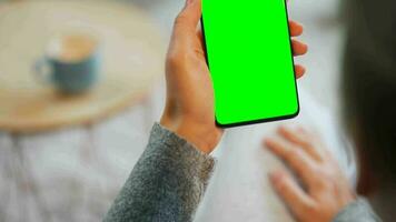 Woman at home using smartphone with green mock-up screen in vertical mode. Girl browsing Internet, watching content video