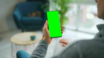 Woman at home using smartphone with green mock-up screen in vertical mode. Girl browsing Internet, watching content video