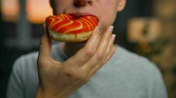 Sweet addiction concept. Woman eats orange donut closeup video