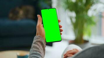 vrouw Bij huis gebruik makend van smartphone met groen mock-up scherm in verticaal modus. meisje browsen internetten, aan het kijken inhoud video
