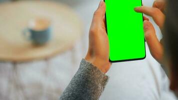 Woman at home using smartphone with green mock-up screen in vertical mode. Girl browsing Internet, watching content video