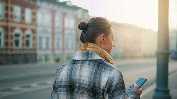 Woman in a coat standing on the street in the early morning and using smartphone video